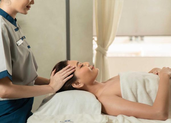 Spa Therapist Performing Head Massage On Woman Laying Down Covered by A Towel
