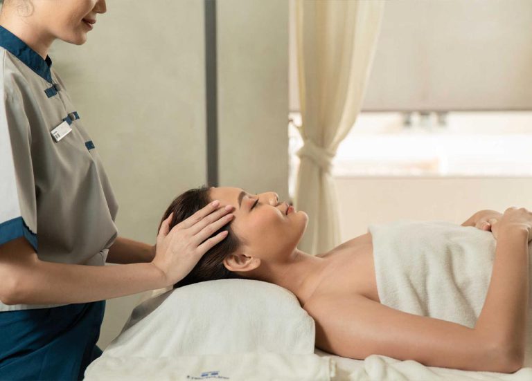 Spa Therapist Performing Head Massage On Woman Laying Down Covered by A Towel