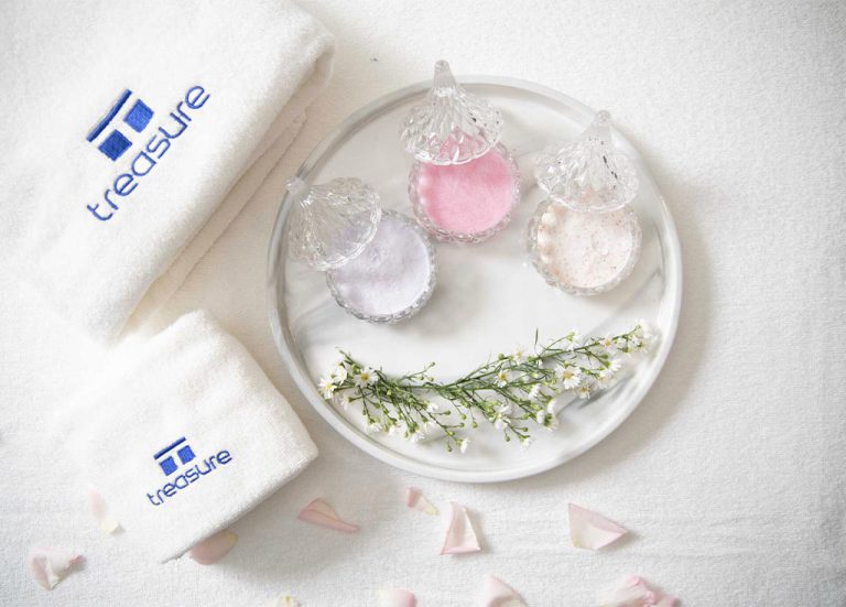 White Towel And Tray Of Body Scrub Products On Light Fabric