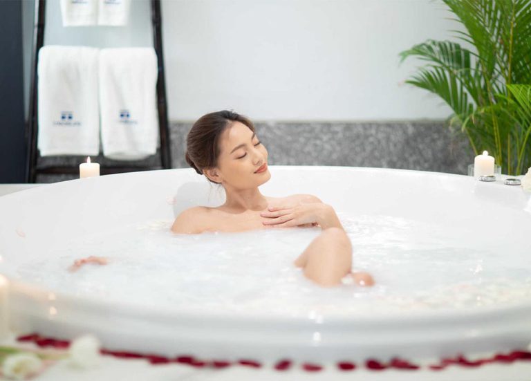 Woman Relaxing At Spa In Bubble Bath Among Rose Petals And Candles