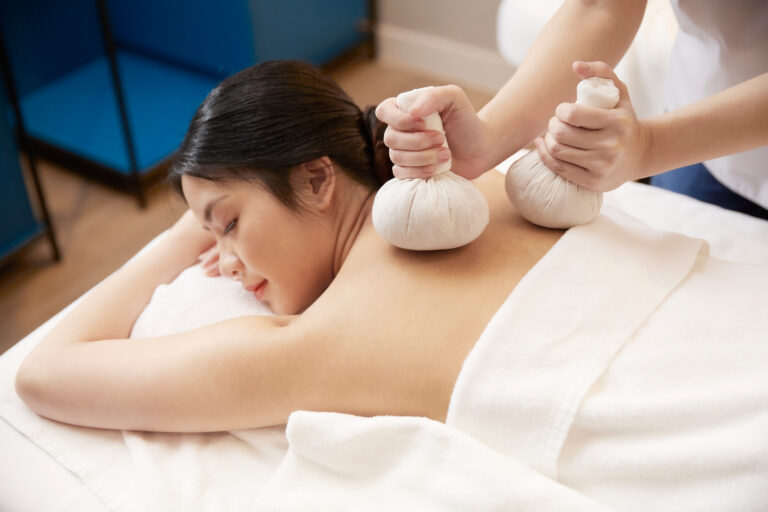 A woman receiving back massage with herbal balls at a spa