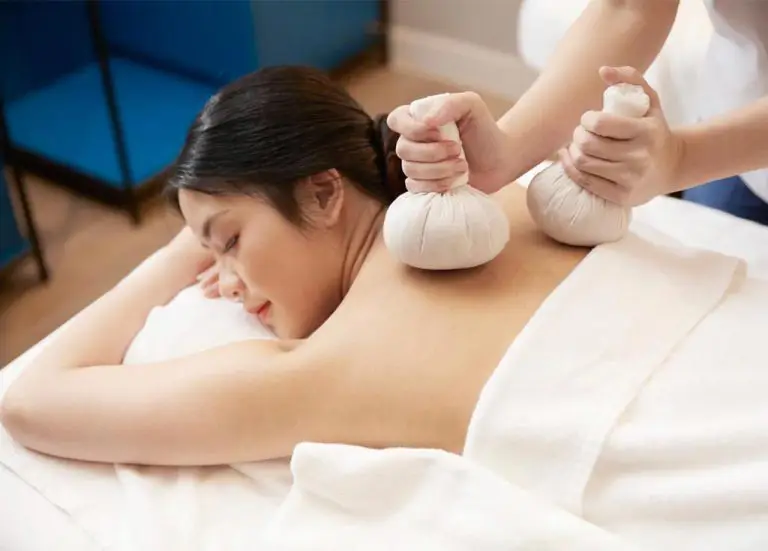 Close-up Of Spa Therapist Performing Herbal Compress Massage On Woman's Shoulders